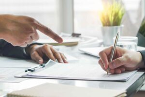 Business partners contract agreement success. Top view of close up hand of bank broker showing to client where to sign signature in contract for housing loan. Document in picture is fake.